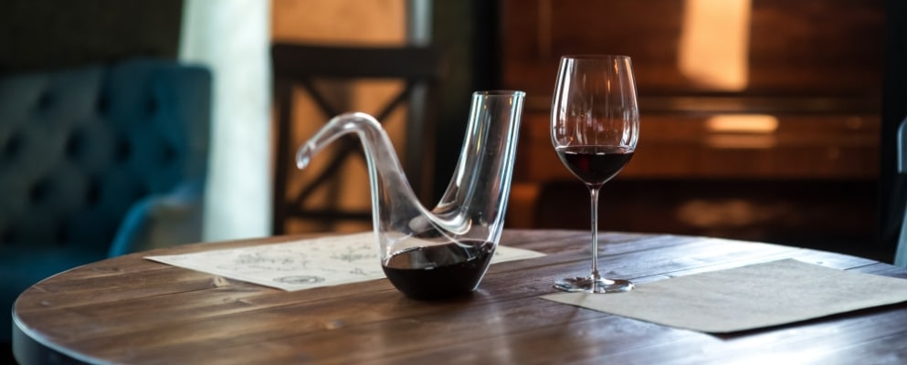a glass & decanter on a table with red wine in them